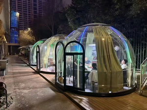 Earth Haven transparent dining pods with curtains, providing a private and luxurious outdoor dining experience at night.