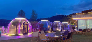 Multiple Nurture pods illuminated transparent pods in an outdoor setting at night, offering a luxurious and ambient glamping experience at Earth Haven.