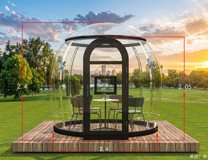 Transparent mini pod with seating area on a wooden deck in a grassy field, perfect for outdoor relaxation or dining at Earth Haven's Nurture Pod Mini.