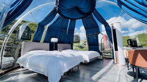 Luxurious outdoor bubble pod with plush bedding and scenic mountain view under blue sky, ideal for glamping and nature retreats at Nurture Pod XL - Earth Haven.