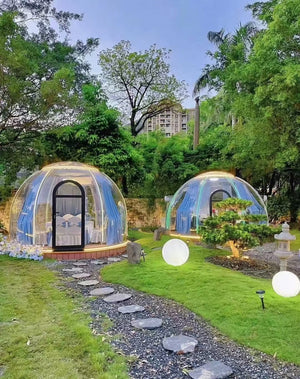 Two transparent outdoor bubble pods in a green garden setting with stepping stones, ideal for luxury glamping and nature retreats at Nurture Pod XL - Earth Haven.