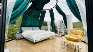 Luxurious eco-friendly glamping pod interior with scenic views, featuring a cozy double bed, modern furnishings, and green drapery in a nature retreat setting